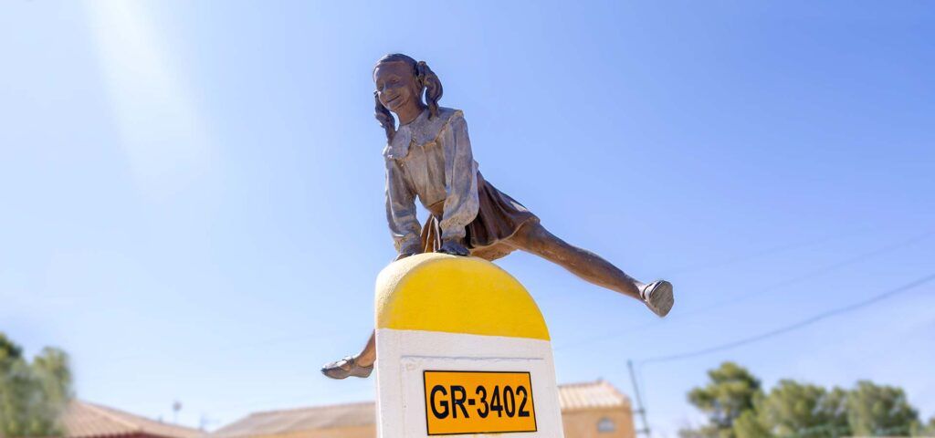 Estatua de la niña saltando un hito kilométrico en Ácula